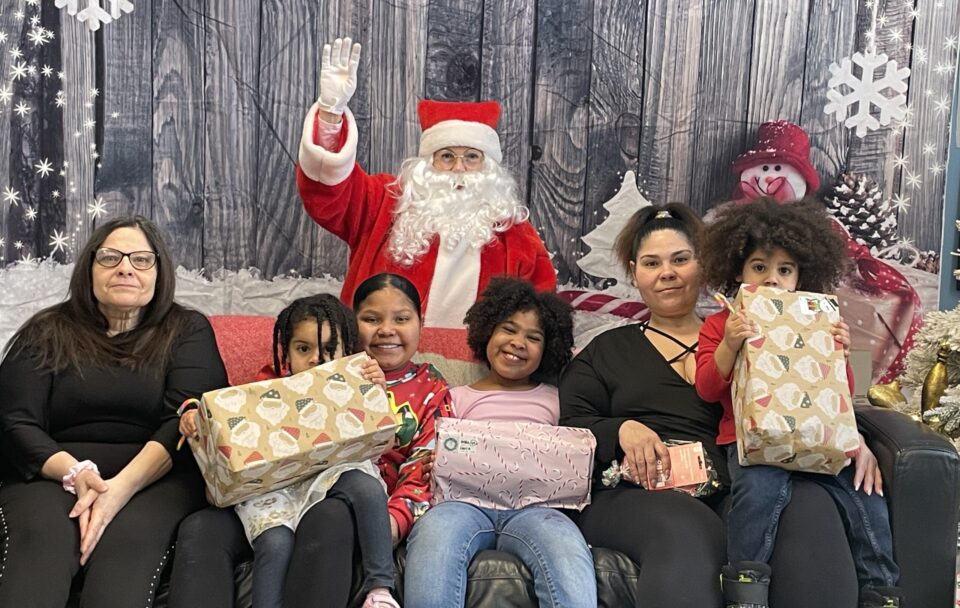 Families with children posing with Santa at Breakfast with Santa 2025, holding wrapped gifts