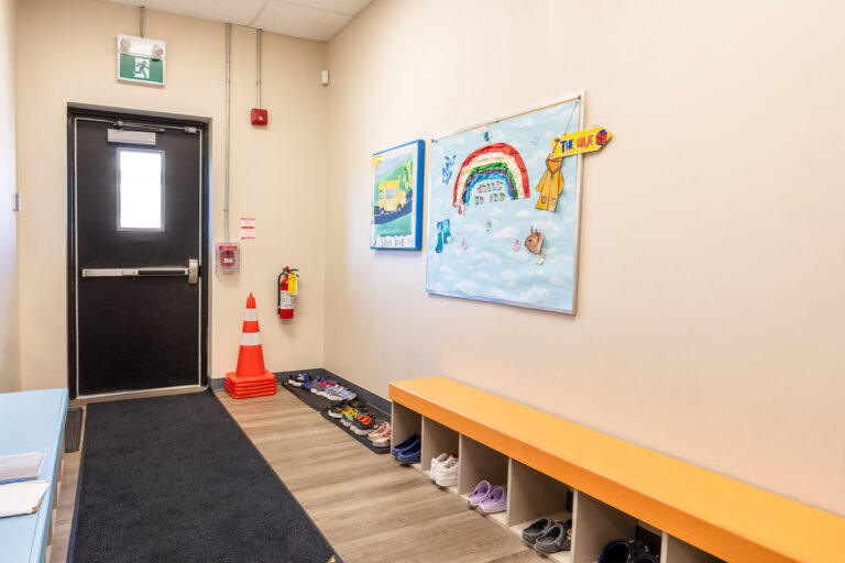 Entrance door at AlphaBee's Etobicoke centre, with a shoe bench and children's rainbow artwork on the wall