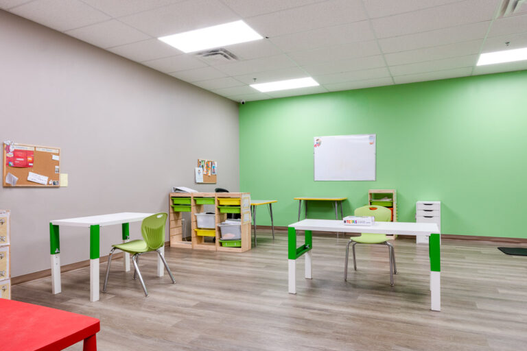 Group room at AlphaBee's Etobicoke centre, with a green feature wall, whiteboard and child-sized tables and chairs