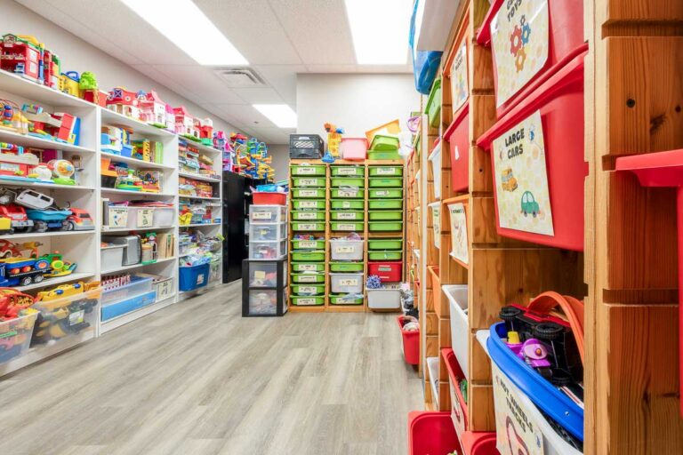 Resource room at AlphaBee's Etobicoke centre, lined with shelves and labelled bins of toys and learning materials
