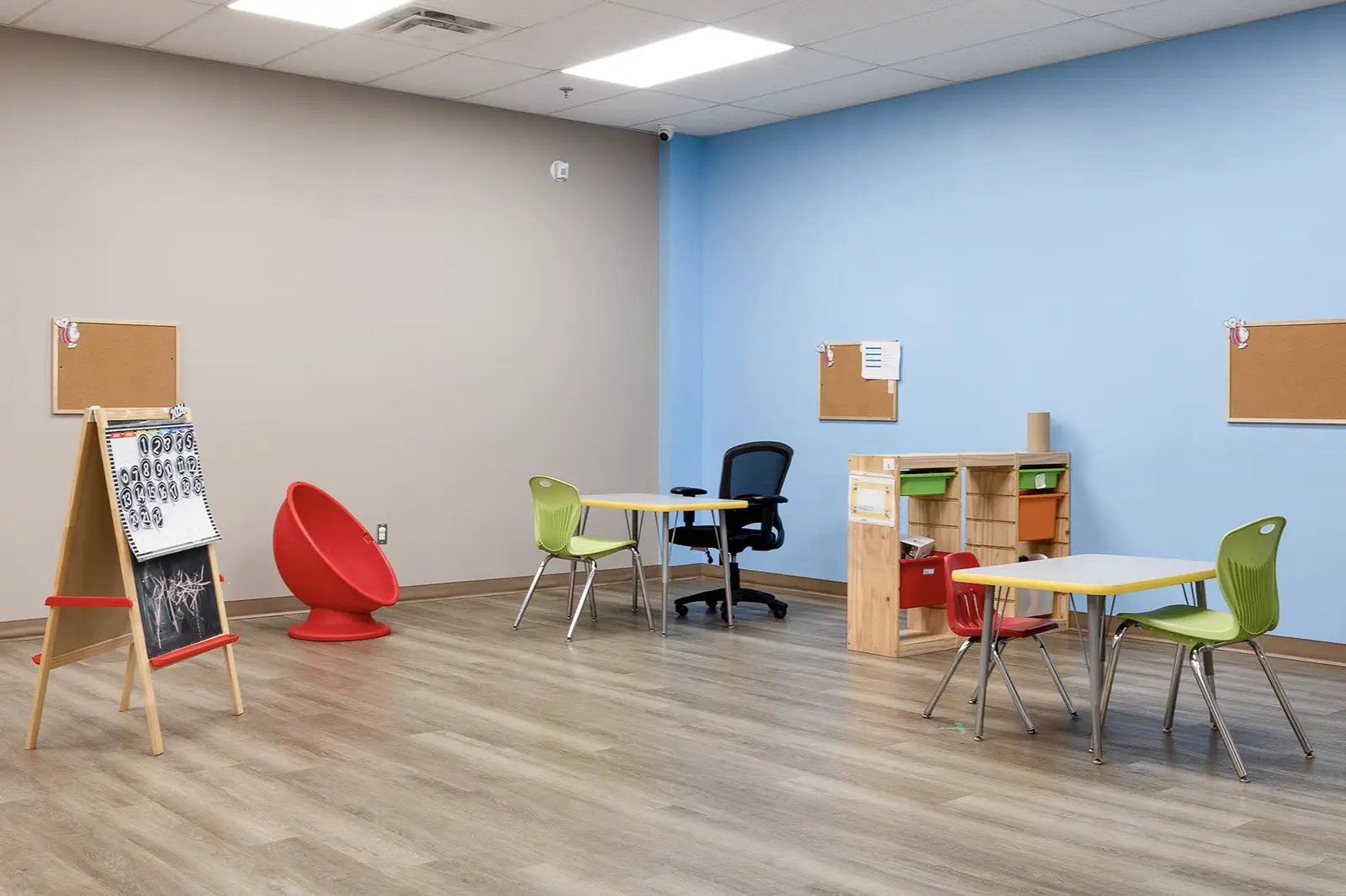 Bright therapy room at AlphaBee Etobicoke with an easel, small tables and a red chair